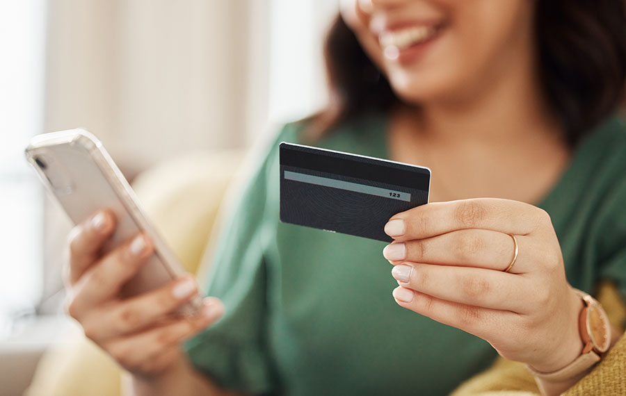 Phone, credit card closeup and woman hands with online shopping and banking at home. Ecommerce, mobile cashback and sale with digital payment and easy pay with discount and smile from web checkout.