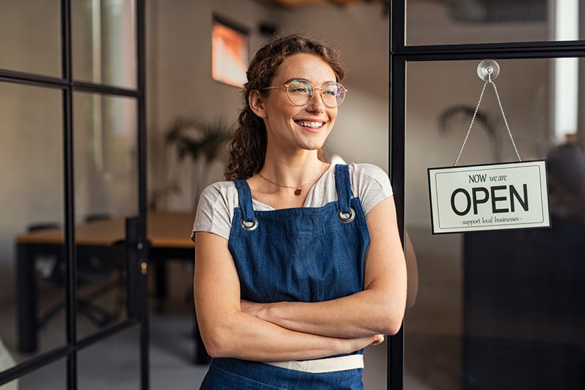 woman smiling at the doors of her business